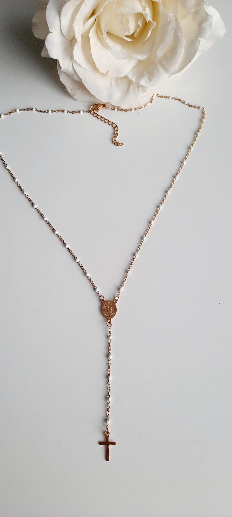 Collier doré en acier inoxydable. Chaine fine incrustée de perles blanches. Sautoir en Y, avec en son centre une médaille gravée, les deux faces sont différentes. Le collier se termine par une fine croix dorée.On adore la finesse de ce bijoux finement travaillé, facile à accorder avec d'autres bijoux. Se porte en soirée ou lors d'évènements moins formels. Absolument tendance