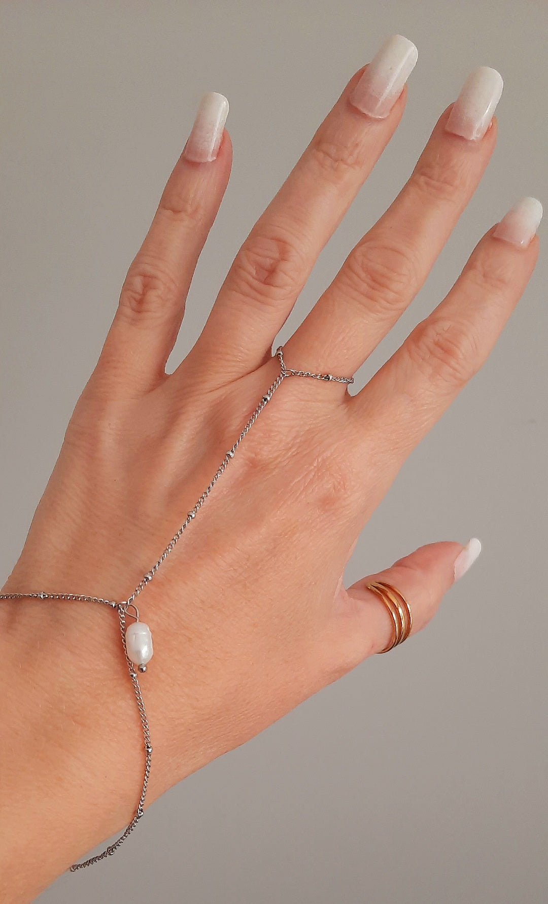 Bracelet de main en acier inoxydable doré ou argenté  Chaine fine à billes qui embellit la main sur laquelle il se glisse avec finesse. Bijoux ornée d'une perle d'eau douce  Terriblement chic, tendance et féminin, on craque pour ce bijoux qui vous accompagnera pour toutes occasions ! Peu de porter à différents doigts en fonction de vos gouts Dimensions : diamètre de l'anneau 1.8cm, longueur de la chaine dessus main 7cm, longueur de la chaine poignet 15+5cm environ. Fermoir en pince de homard